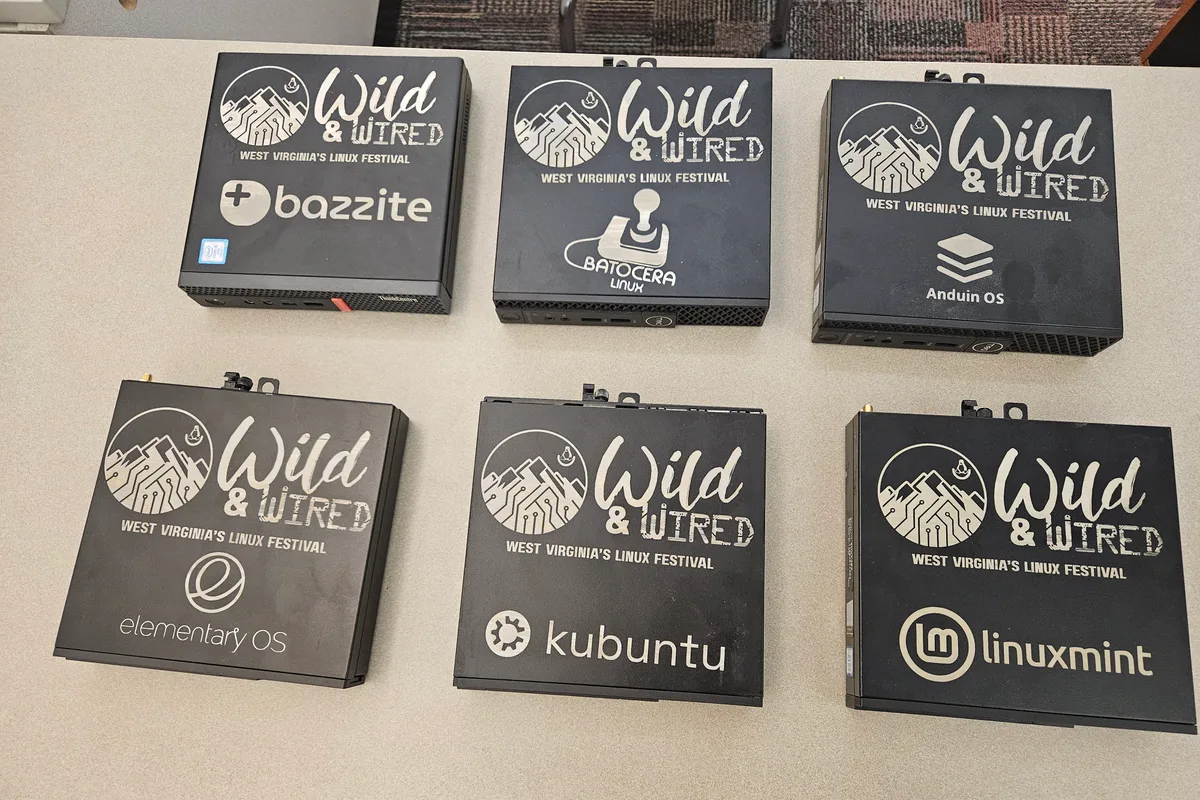 Six small black desktop machines laid out on a table, each lid etched with the Wild and Wired mark and the name of the Linux version it runs