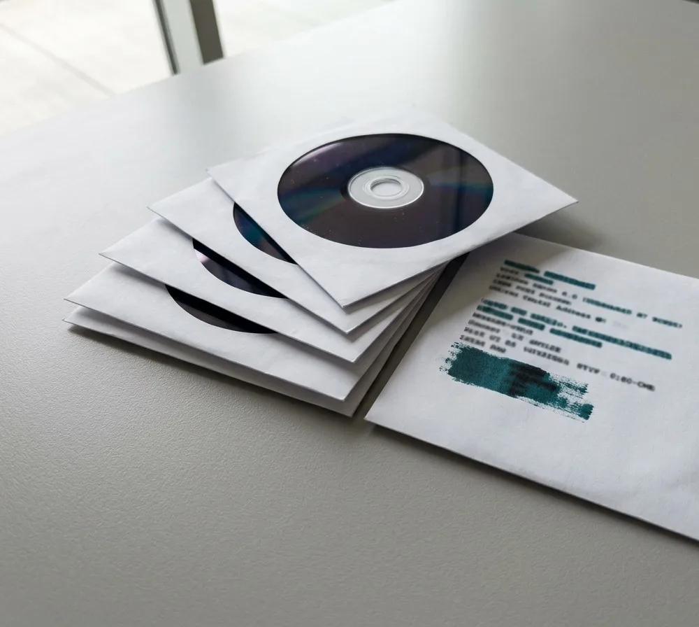 Three burned discs in white paper sleeves on a wooden table, with a printed checksum line visible on the nearest sleeve